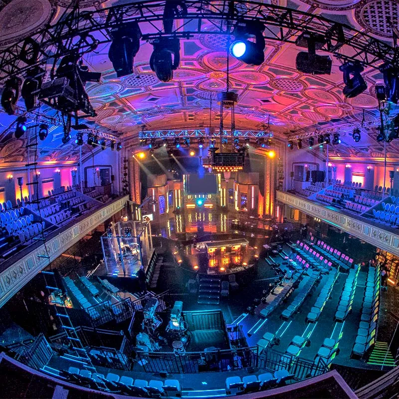 An expansive auditorium with a prominent stage illuminated by lights, offering ample seating for an audience.