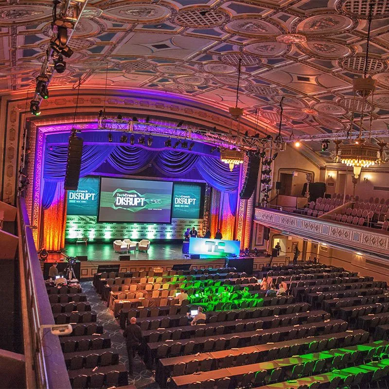 A spacious auditorium featuring a stage and a large screen, designed for presentations and performances.