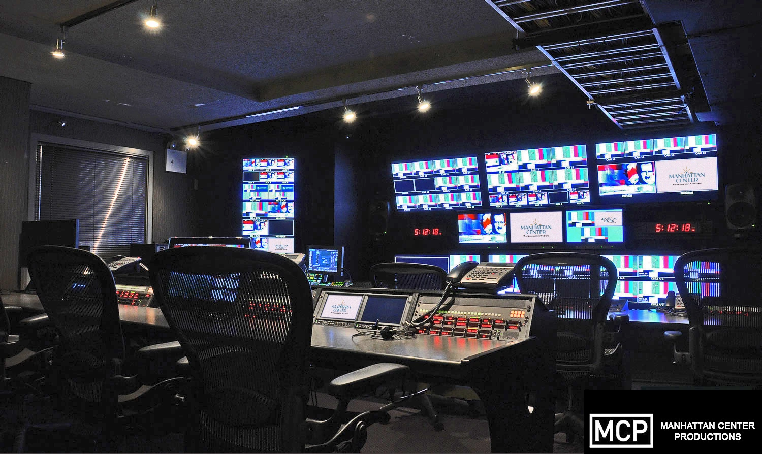 A modern audio control room featuring a large mixing console, multiple screens, sound equipment, and a swivel chair