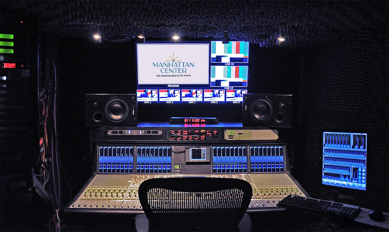 A modern audio-visual control room featuring monitors, sound equipment, and a mixing console, branded with the Manhattan Center logo