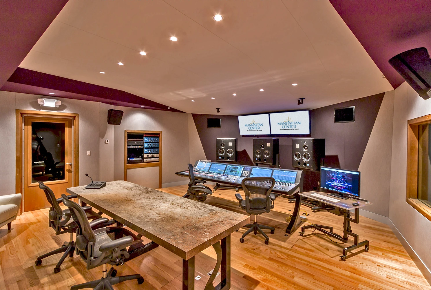 mc audio studio 7 lrg 2025-logo (2) A modern music studio featuring a large mixing console, multiple audio monitors, and screens displaying sound levels